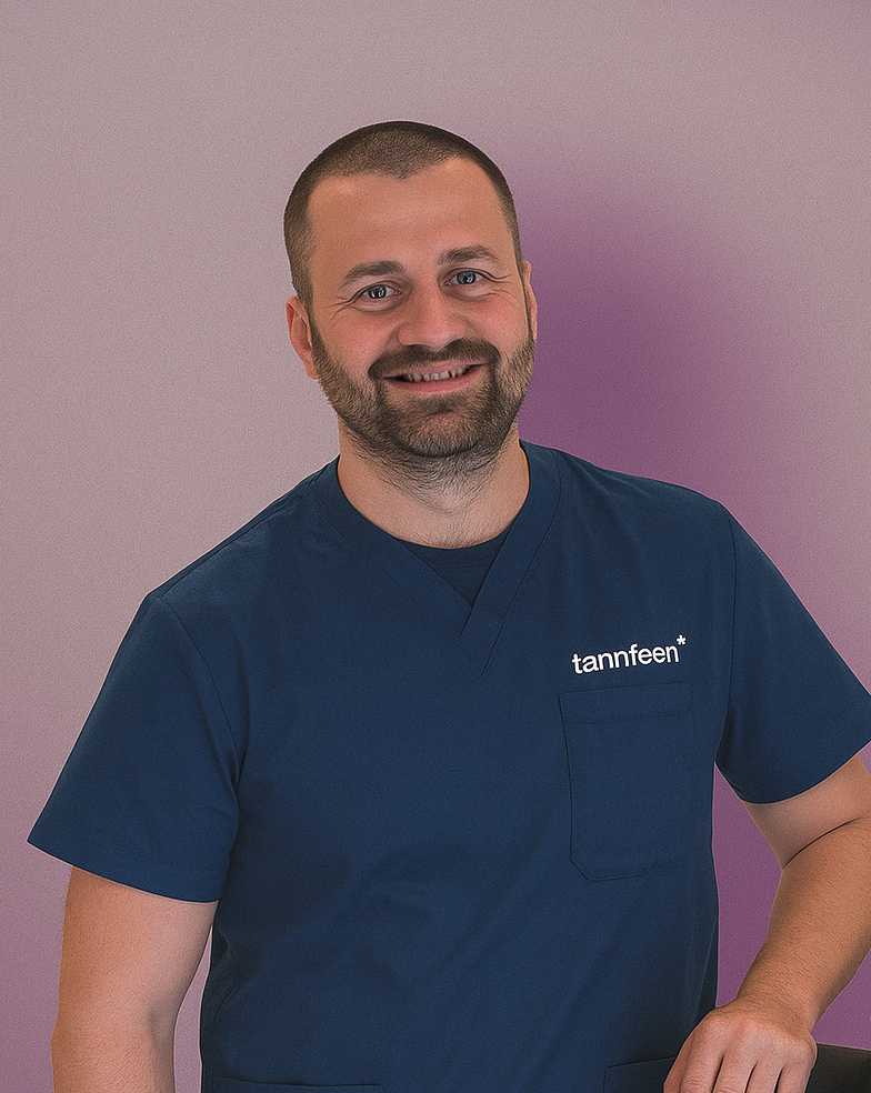 Smilende mann i marineblå klinikkuniform står foran en rosa-lilla gradientbakgrunn; på brystet står det «tannfeen» ved lommen.